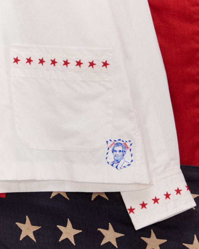 The Red Star Long Sleeve Shirt features red stars on the pocket and cuff with a blue Abe Lincoln patch, ideal for Liberty costumes or Fourth of July festivities, set against a starry background.