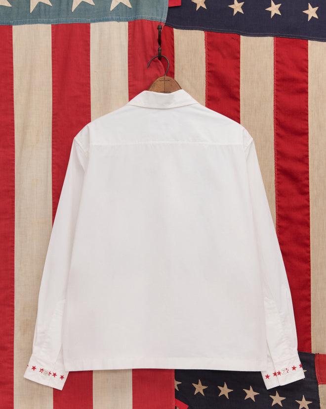 A Red Star Long Sleeve Shirt hangs against an American flag-patterned backdrop—ideal for Liberty costumes or celebrating the Fourth of July.