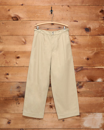 Wide Leg Snap Trousers - Khaki hanging on a wooden hanger against a rustic wooden wall background, featuring a wide-leg silhouette and side buckle waist adjusters.
