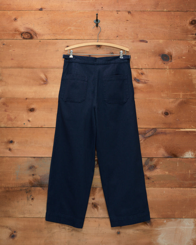 Wide Leg Snap Trousers - Navy, featuring a vintage Australian military style and back pockets, hang on a wooden wall.