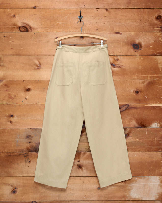 Wide Leg Snap Trousers - Khaki with side buckle waist adjusters, hanging on a wooden hanger against a rustic wooden wall.