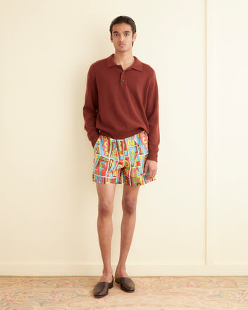 A person in a rust-colored long-sleeve 100% cotton shirt and New England Mosaic Shorts stands against a cream wall on vintage upholstery.