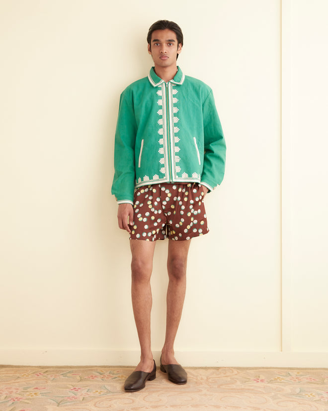 A person in a green jacket and Bubble Dot Boxers, inspired by 1930s-1940s fashion, stands against a cream wall, showcasing an overlapping dots pattern reminiscent of vintage elegance.