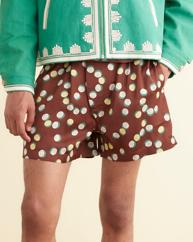 A person in a green jacket and Bubble Dot Boxers, inspired by 1930s-1940s fashion, stands against a cream wall, showcasing an overlapping dots pattern reminiscent of vintage elegance.