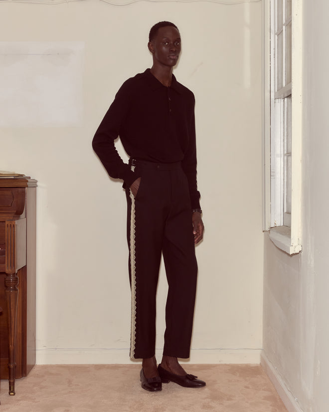 A person in Lacework Side-Buckle Trousers stands indoors near a window with one hand in their pocket.