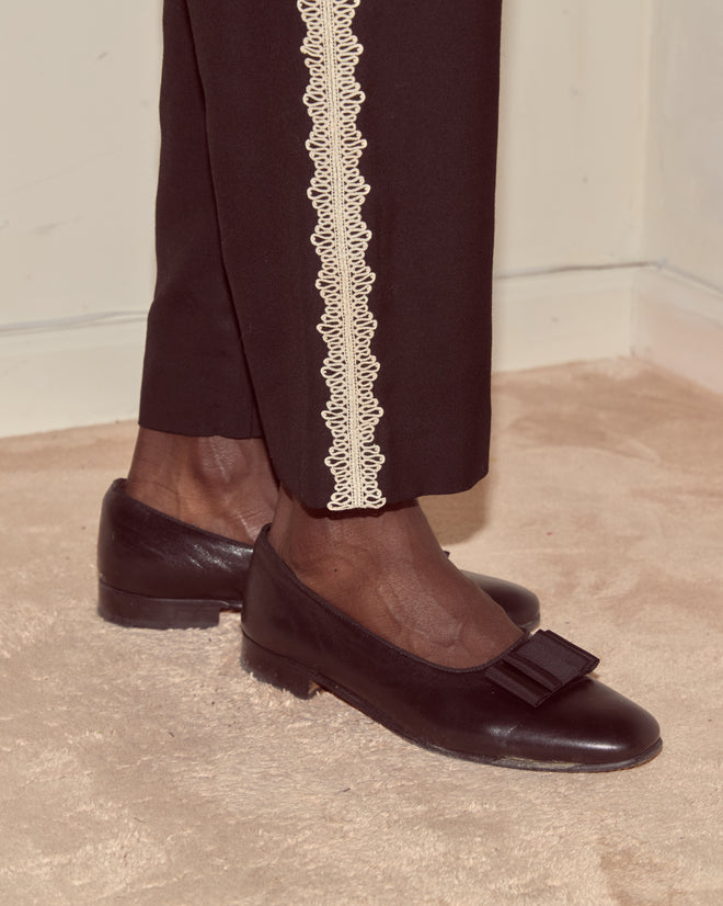 Person wearing Lacework Side-Buckle Trousers and black bow flats, standing on a beige carpet.
