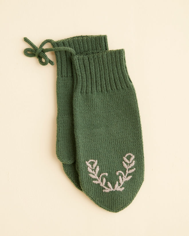 The Floret Mittens - Green showcase a white embroidered leaf pattern on a light beige background, expertly crafted with soft merino wool for enhanced warmth and comfort.