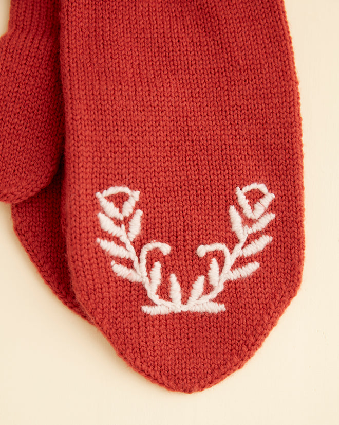 Floret Mittens - Red, handmade with a white embroidered floral design on one mitten, placed against a plain beige background.