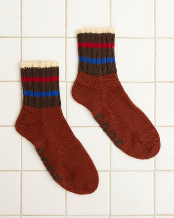 The Herrington Stripe Socks - Brown, hand-knit from merino wool, feature blue and red stripes and are displayed on a tiled white background.