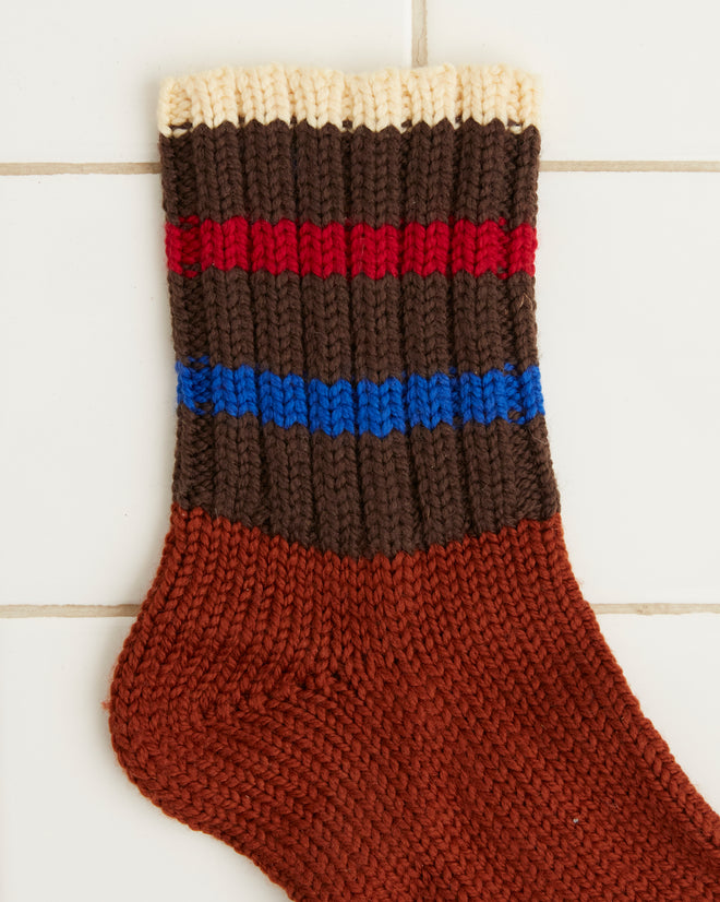 The Herrington Stripe Socks - Brown, hand-knit from merino wool, feature blue and red stripes and are displayed on a tiled white background.