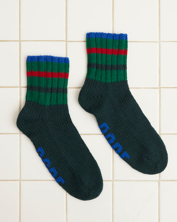 The Herrington Stripe Socks in green, adorned with blue, red, and green stripes around the ankle, rest elegantly on a tiled floor.