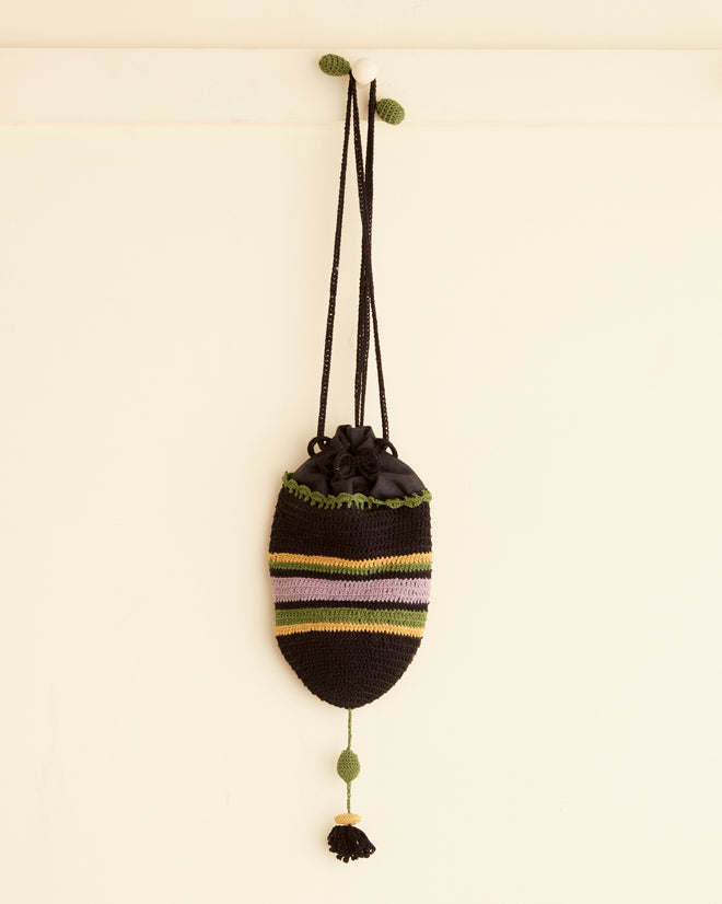 The Harbor Stripe Bag, an enchanting crochet reticule adorned with multicolored stripes and a tassel, hangs gracefully on a wall.