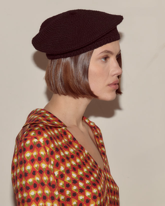 Woman wearing a black Crochet Beret and a patterned shirt, with a bob haircut, facing right.