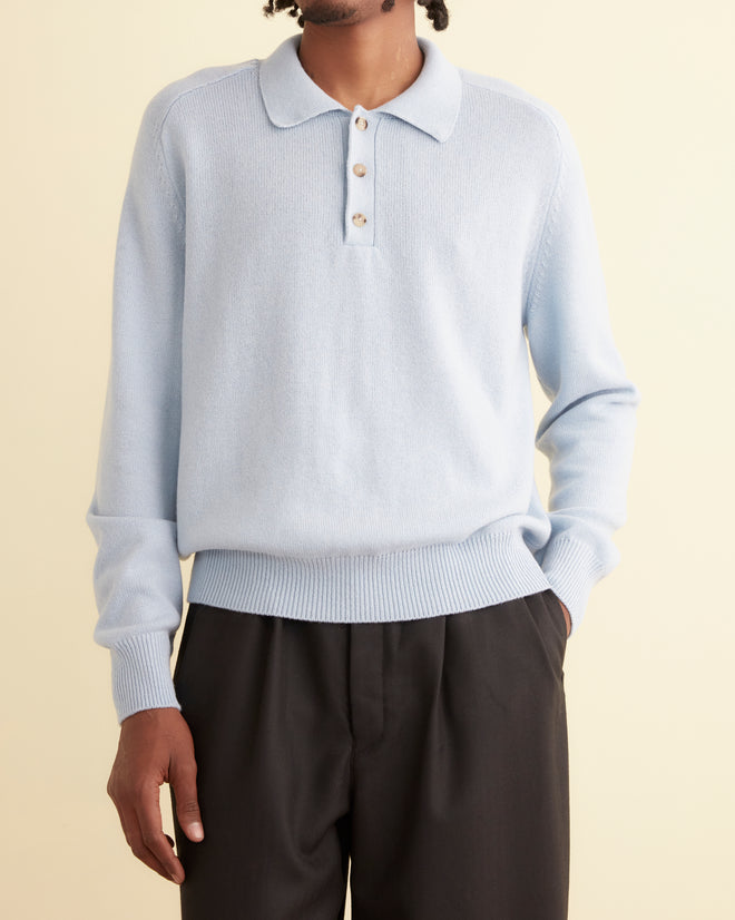 A person in a light blue Cashmere Polo sweater with buttons and black pants is standing against a plain background.