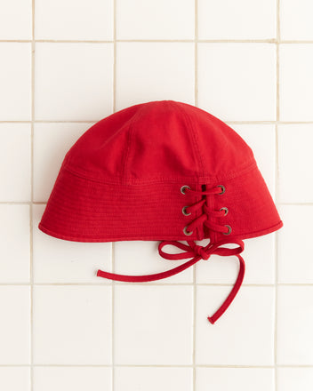 The red Spring Twill Sailor Cap features a lace-up detail and is showcased against a white tiled background.