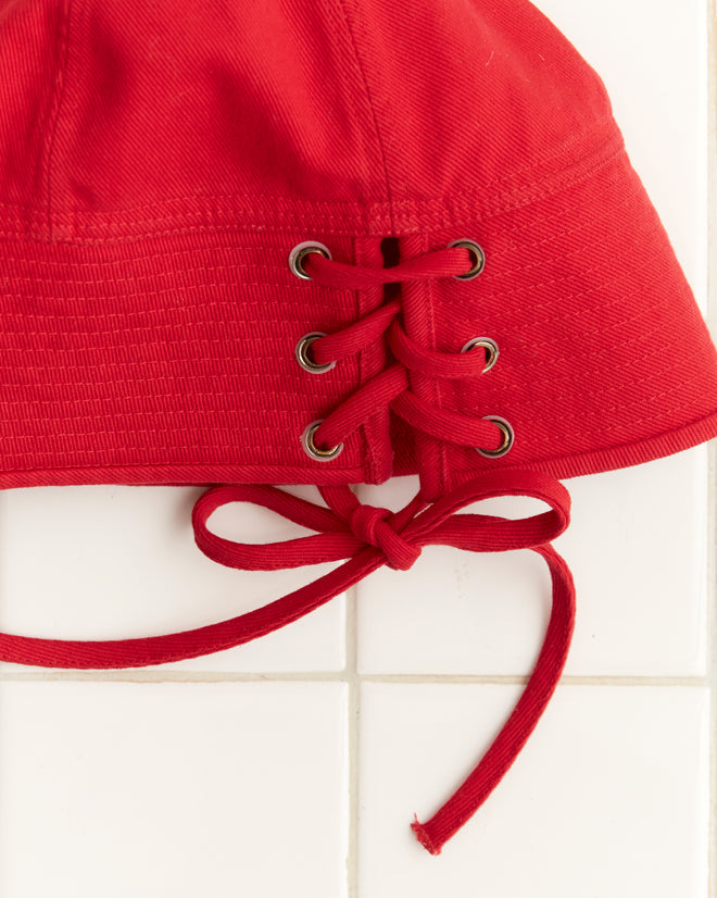 Close-up of the Spring Twill Sailor Cap in red, featuring lace-up details and eyelets, on a tiled surface.