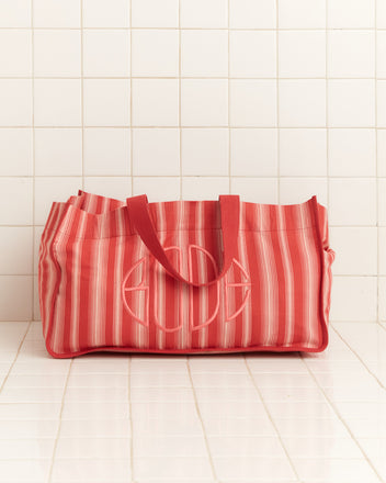 The Parasol Stripe Tote features red and white awning stripes, sturdy handles, and an embroidered Bode logo, displayed on a tiled white surface with a tiled wall backdrop.