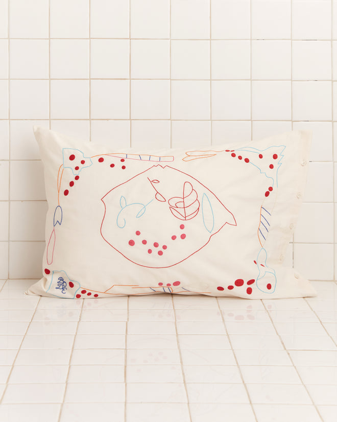 The Garden Party Pillowcases, featuring abstract red and blue line drawings, rest against a white tiled wall in soft linen.