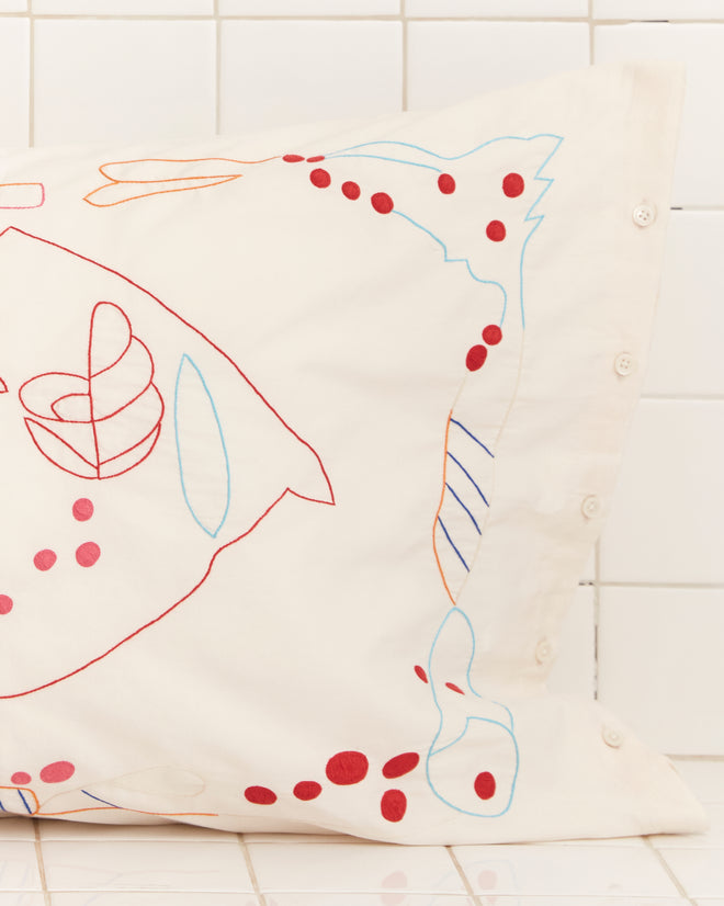 The Garden Party Pillowcases feature elegant white linen with abstract red, blue, and orange embroidery, set against a tiled background.