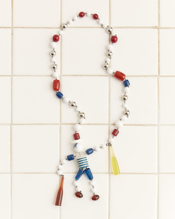 The Trinket Man Necklace, a vibrant Bakelite piece, features colorful beads and a figure charm elegantly arranged on a tiled background.