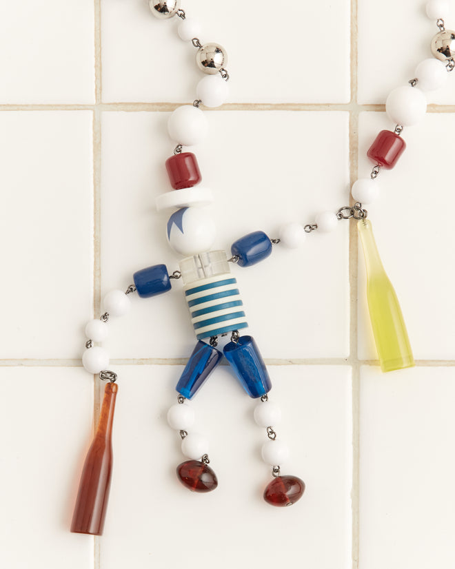 A Trinket Man Necklace with a person-shaped pendant adorned with colorful beads and bottle charms in vibrant red, blue, and white is elegantly displayed on a tiled surface.