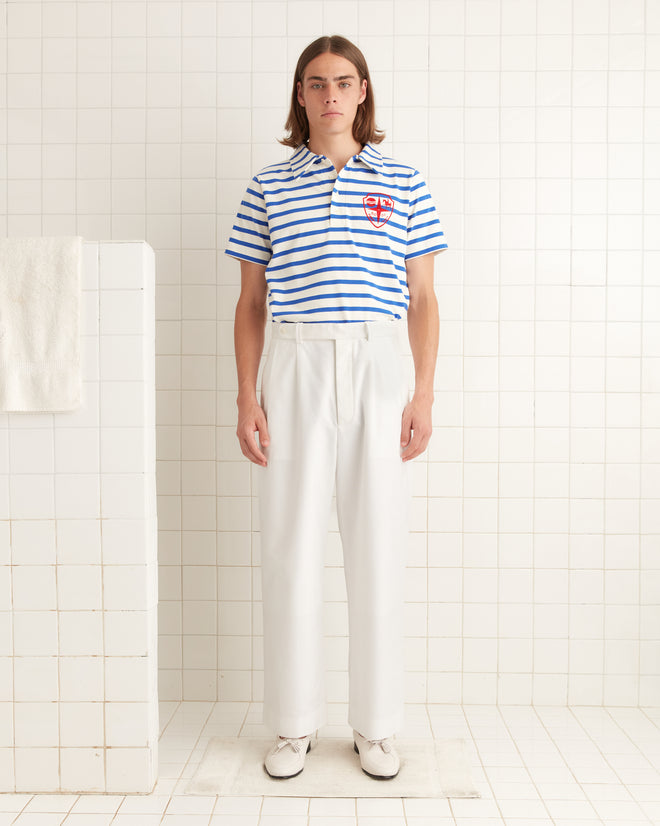 Someone in a blue striped shirt and Piqué McNab Trousers stands in a tiled room, with the wide-leg fit adding an effortless touch of style.