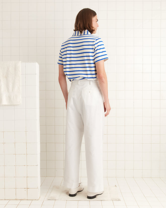 A person in a blue and white striped shirt and Piqué McNab Trousers stands in a tiled room, facing away.
