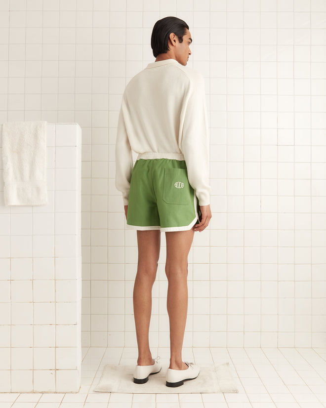 A person in a white sweater and Euro Gym Shorts stands on a mat in a white tiled room, facing away.