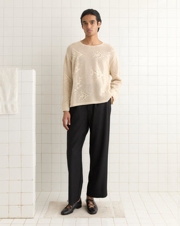 A person wearing an Angel Fish Pullover and black pants stands in a tiled room near a white towel, exuding 1970s-inspired vibes.