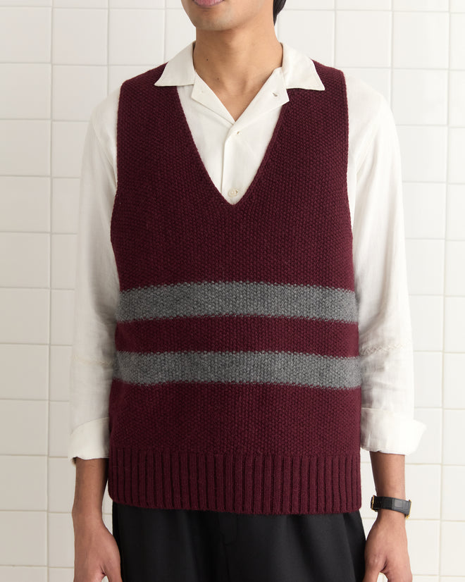 A person in a Collegiate Vest with gray stripes over a white shirt and black pants stands against a tiled wall.