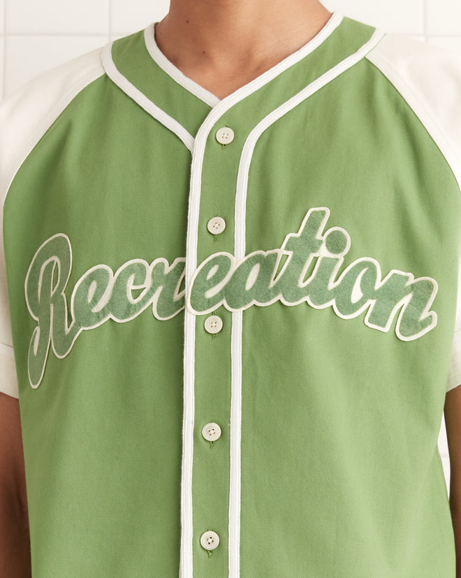 Someone wears the Outfield Baseball Shirt, a green and white jersey with "Recreation" on the front and a classic striped trim inspired by 1940s baseball uniforms.