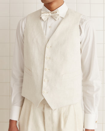 A person wearing the Nelson Brookline Waistcoat, styled in a cream linen suit and bow tie reminiscent of the 1940s-1950s, stands against a tiled background.