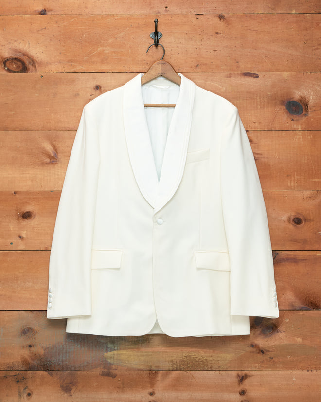 Meringue Shawl Collar Tuxedo Jacket in ivory wool, featuring a classic shawl collar, displayed on a wooden hanger against a rustic wooden wall background.