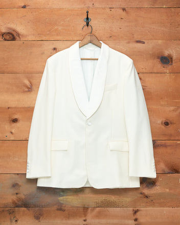 Meringue Shawl Collar Tuxedo Jacket in ivory wool, featuring a classic shawl collar, displayed on a wooden hanger against a rustic wooden wall background.