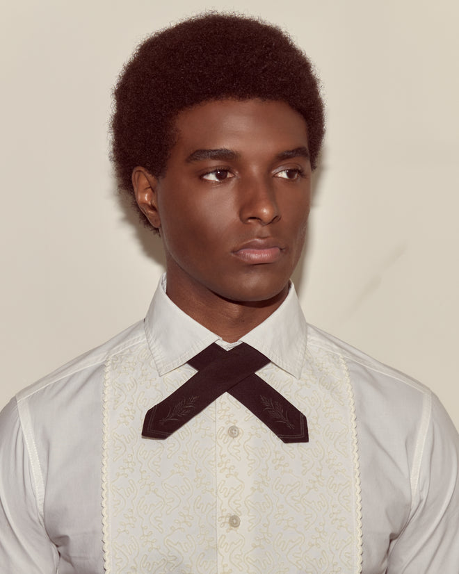 A man in a white shirt wears the Meadow Cross Tie in black, looking to the side against a plain background.