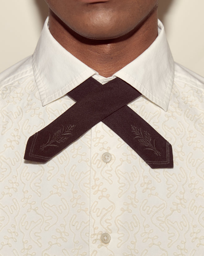 A person wearing a white patterned shirt with the Meadow Cross Tie - Black, featuring embroidered leaves and crossed neatly at the neck.