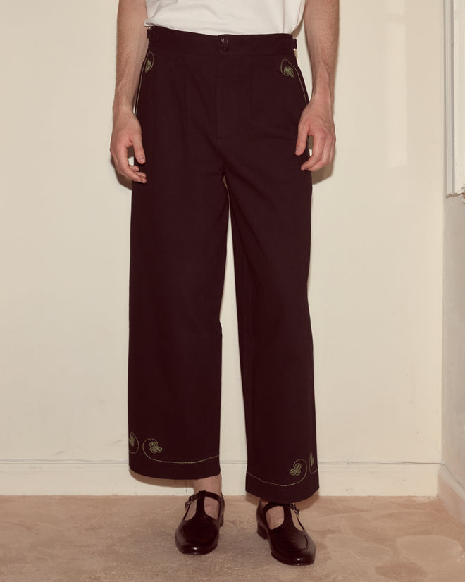 A person wearing Lucky Draw Trousers—black hand-embroidered cotton with antique tablecloth-inspired hem detailing—paired with black shoes.