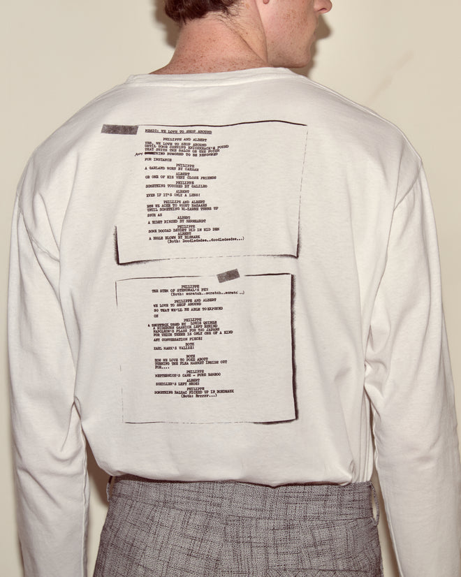 A person wearing a white Script Tee featuring black text and graphics printed on the back.
