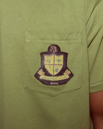 The Theatre Patch Tee is a green shirt with a chest pocket that features a bullion patch crest labeled 