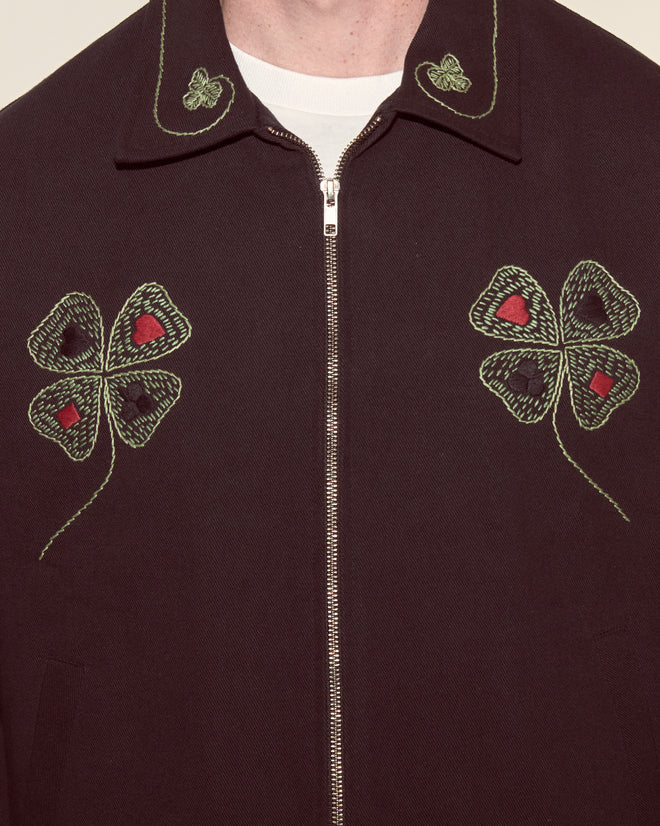 Close-up of the Lucky Draw Jacket, a classic workwear piece adorned with green, hand-embroidered clovers and hearts on the chest and collar, inspired by playing card motifs.