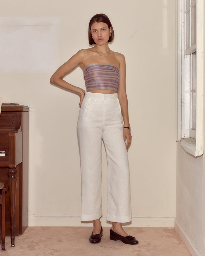 Indoors by a piano, a woman wearing a striped tube top, white pants, and black shoes accessorizes with the Cheshire Scarf.