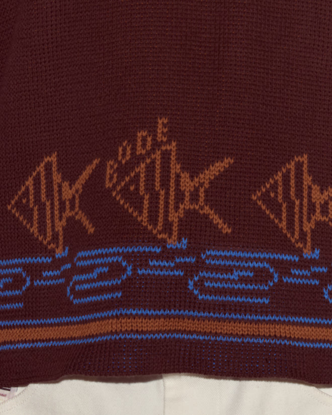 The Fish School Sweater is a knitted cotton sweater with brown fish patterns and blue wave designs set against a maroon background.
