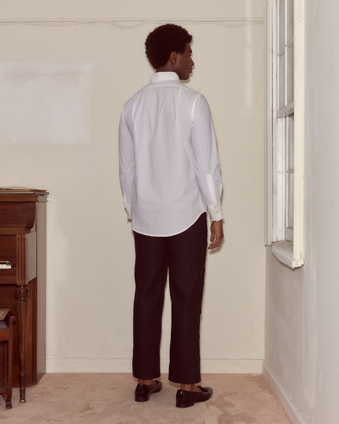 Wearing a Closerie Tuxedo Shirt and black pants, a person stands indoors with their back to the camera, facing a window.