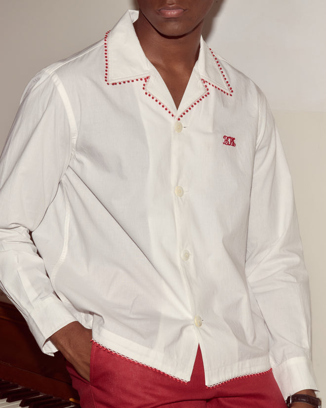 Man wearing a Redbud Long Sleeve Shirt with red stitching and Bode monogram, paired with red pants, standing near a piano.