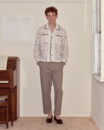 A man stands indoors by a piano, wearing the Blackberry Patch Long Sleeve Shirt, beige pants, and dark loafers.