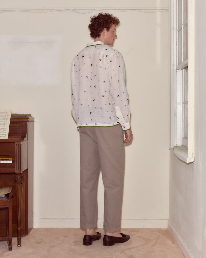 A man with curly hair stands facing a corner, wearing the Blackberry Patch Long Sleeve Shirt, beige pants, and black loafers.