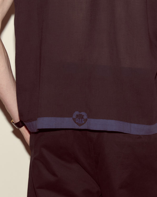 A person wearing the Heart Deco Short Sleeve Shirt in navy/black, featuring a sheer cotton voile fabric and a small circular logo near the hem.