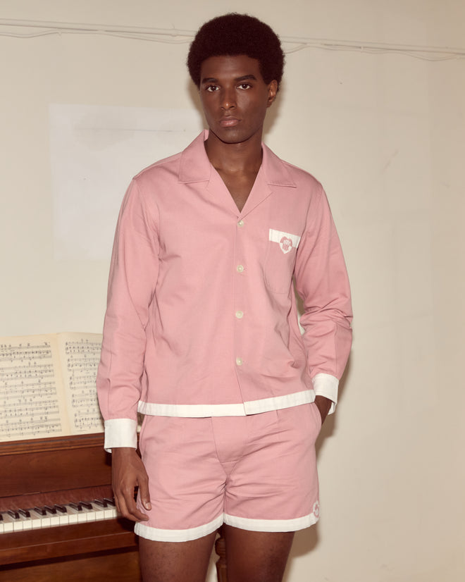 A person in a pink pajama set with the Heart Deco Long Sleeve Shirt stands by a piano with sheet music, looking at the camera.