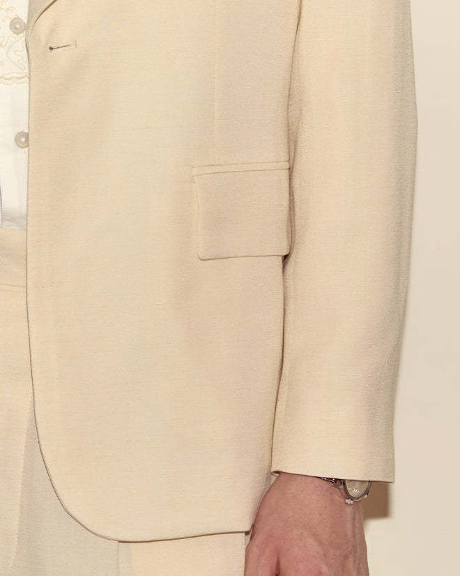 A person wearing the Slub Weave Tuxedo Jacket in a cream viscose linen blend with a shawl collar, paired with a white shirt and a silver wristwatch.