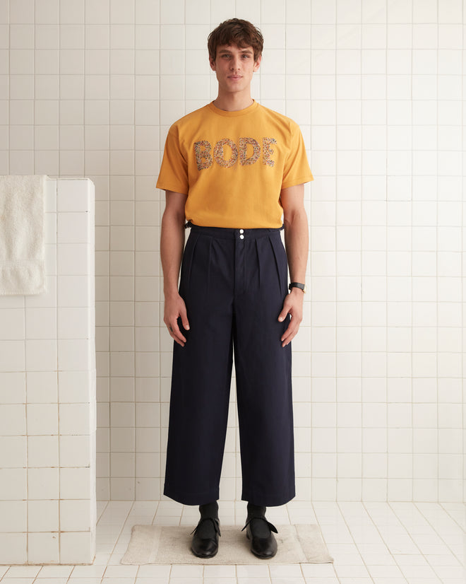 A person stands indoors against a plain wall, sporting the Multi Bead Tee—a yellow children’s novelty t-shirt with the word 